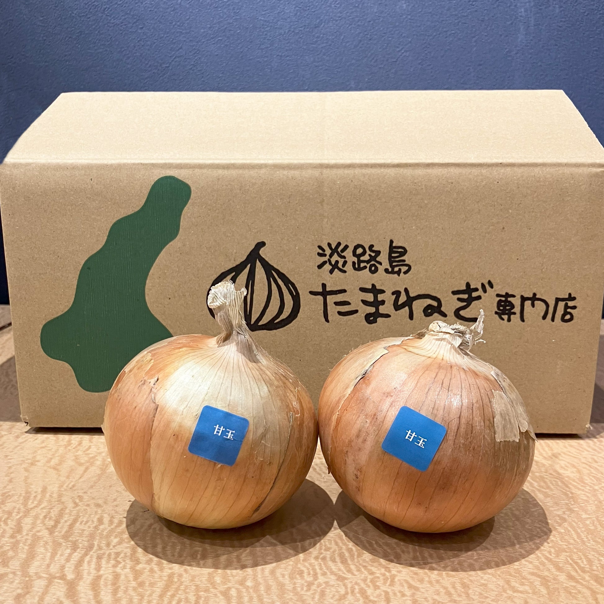 淡路島たまねぎ専門店のロゴが入った段ボールの前にたまねぎを２個並べています
